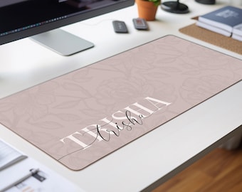 May include: A rectangular desk mat in a dusty rose color featuring a subtle, tonal floral line art pattern. The name "Trisha" is printed across the center in a combination of bold white block lettering and a delicate black cursive script font.