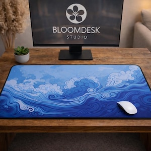May include: A blue and white mouse mat featuring a wave design, a white mouse, and a computer monitor displaying the text "BLOOMDESK STUDIO". The mat is on a wooden desk.