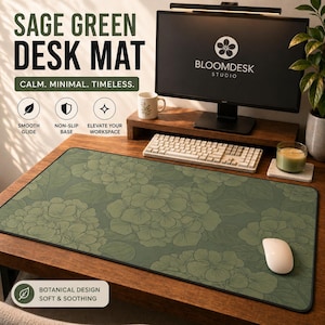 May include: A rectangular sage green desk mat featuring a repeating botanical pattern of hydrangea flowers in a darker shade of green. The mat has a smooth surface, a black stitched edge, and a non-slip base, displayed on a wooden desk surface.