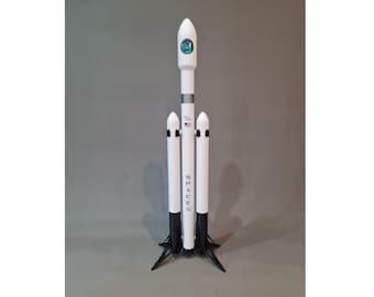 Könnte beinhalten: Ein weißes Modell einer SpaceX Falcon 9 Rakete mit drei Boostern und einer schwarzen Basis. Die Rakete trägt das SpaceX Logo und die Worte "SpaceX" auf der Seite.