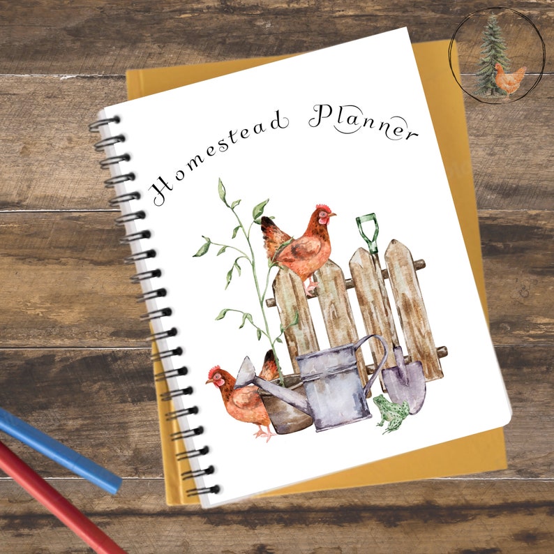 K&ouml;nnte beinhalten: Ein wei&szlig;es Spiralnotizbuch mit dem Text "Homestead Planner" in brauner Kursivschrift. Der Umschlag zeigt eine Aquarell-Illustration von zwei H&uuml;hnern, die auf einem Holzzaun sitzen, mit einer Gie&szlig;kanne, einer Schaufel und einem Frosch.
