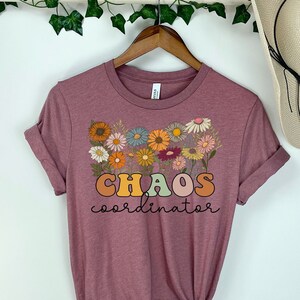May include: Mauve t-shirt with a floral design and the text "CHAOS coordinator" in rainbow colors.