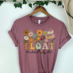 May include: Mauve short-sleeved t-shirt with a floral design and the text "FLOAT nurse" in rainbow colors.