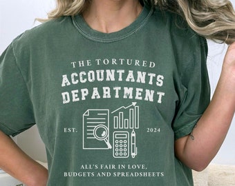 May include: A green t-shirt with a white graphic design that says "The Tortured Accountants Department" with a magnifying glass, calculator, and pencil. The graphic also includes the text "Est. 2024" and "All's fair in love, budgets and spreadsheets".