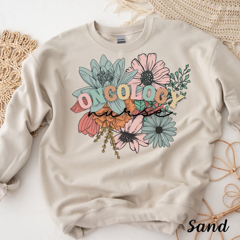 May include: A sand-colored sweatshirt with a floral design and the text "ONCOLOGY nurse" in colorful letters.