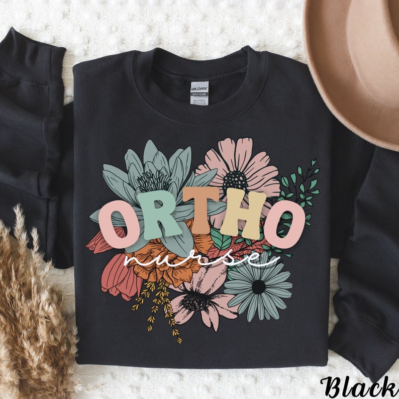 Peut inclure: Sweat-shirt noir avec un motif floral et le texte "ORTHO nurse" en lettres color&eacute;es.