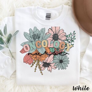 May include: White sweatshirt with a floral design and the words "ONCOLOGY NURSE" in colorful letters.