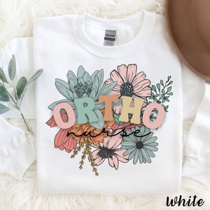 Peut inclure: Sweat-shirt blanc avec un motif floral et le texte "ORTHO nurse" en lettres color&eacute;es.