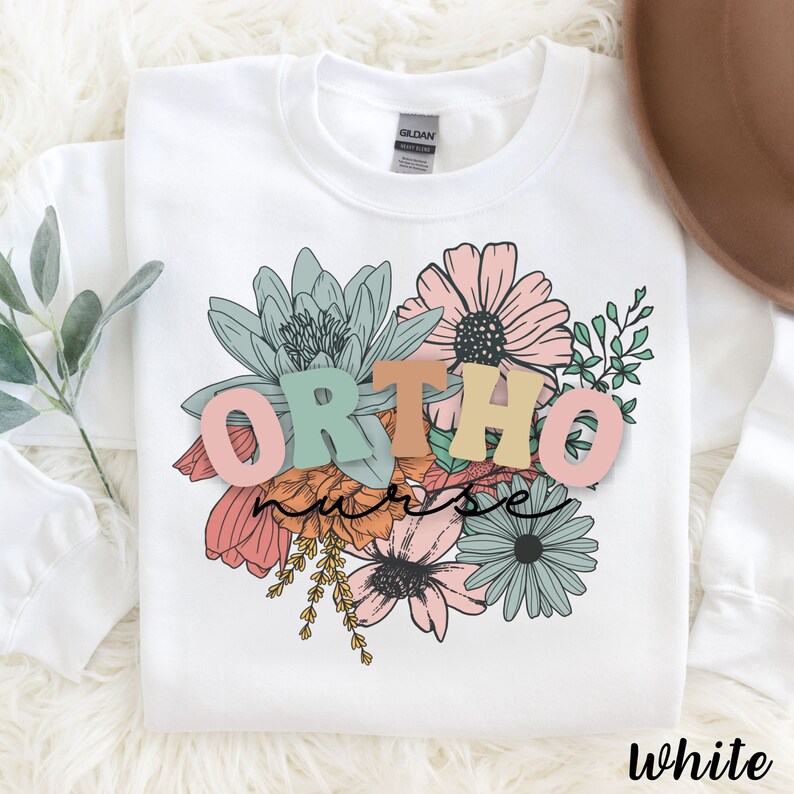 Peut inclure: Sweat-shirt blanc avec un motif floral et le texte "ORTHO nurse" en lettres color&eacute;es.