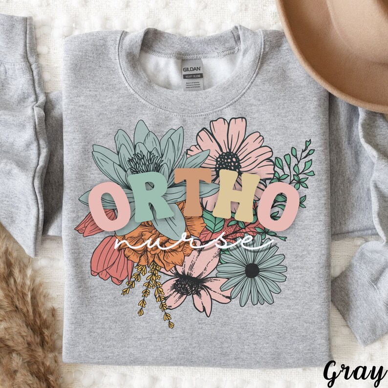 Peut inclure: Sweat-shirt gris avec un motif floral et le texte "ORTHO nurse" en lettres color&eacute;es.