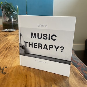 以下が含まれることがあります： 「What is MUSIC THERAPY?」というタイトルの白い本。著者はCameron Wood, MT-BC。表紙には白黒のアコースティックギターの画像が載っている。