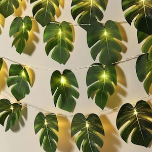 May include: String of lights with green leaf-shaped paper lanterns. The lights are strung on a clear wire and the leaves are evenly spaced.