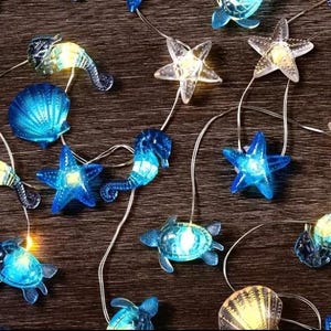 May include: String of decorative lights featuring sea creatures like seahorses, starfish, and turtles. The lights are blue and clear, with a warm glow. The string is silver, and the background is a dark wood.