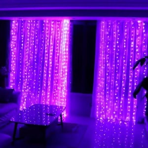 May include: Two sets of purple fairy lights strung across a room, creating a curtain effect. The lights are strung on a clear wire and emit a soft, warm glow.