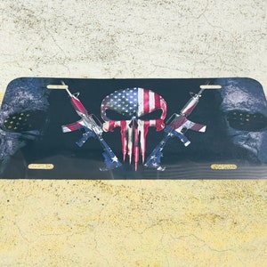 Puede incluir: Una calavera en blanco y negro con un diseño de bandera estadounidense, rifles cruzados y un fondo desgastado. La calavera tiene un diseño rojo y blanco en la parte superior de la cabeza. Los rifles están cruzados detrás de la calavera. El fondo es un diseño desgastado en blanco y negro.