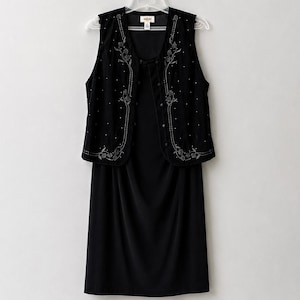 May include: A black sleeveless dress paired with a matching black vest. The vest features a decorative floral embroidery pattern in silver thread along the front panels and is accented with small, scattered silver beads throughout the fabric.