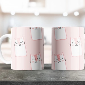 Op de afbeelding: Twee witte keramische mokken met roze handvatten en een roze achtergrond met een herhalend patroon van witte katten met gesloten ogen.