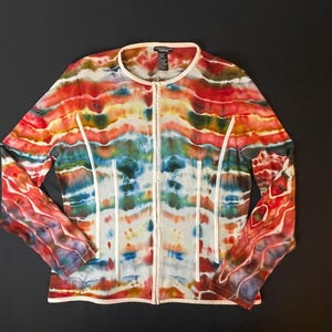 Könnte beinhalten: Eine Jacke mit Reißverschluss und einem lebendigen Batikmuster in Rot-, Orange-, Gelb-, Blau- und Grüntönen. Die Jacke hat einen weißen Besatz am Kragen, an der Vorderseite und entlang der Nähte. Die Ärmel sind lang.