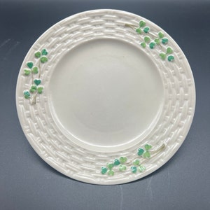 May include: A white ceramic plate with a woven pattern and green shamrock designs around the edge.