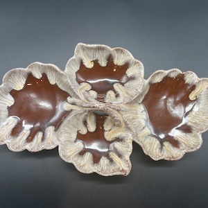 May include: A brown and white ceramic serving dish with three sections shaped like leaves. The dish has a glossy finish and a unique swirl pattern.
