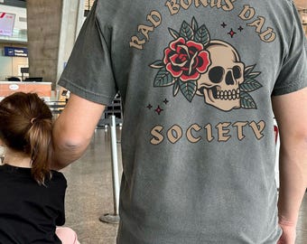 May include: A gray t-shirt with a skull and rose graphic and the text "Rad Bonus Dad Society".