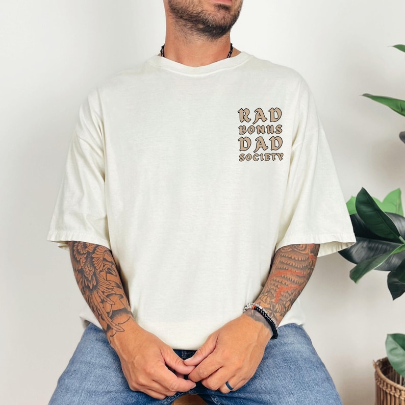 May include: A white t-shirt with a brown graphic print that says "Rad Bonus Dad Society".