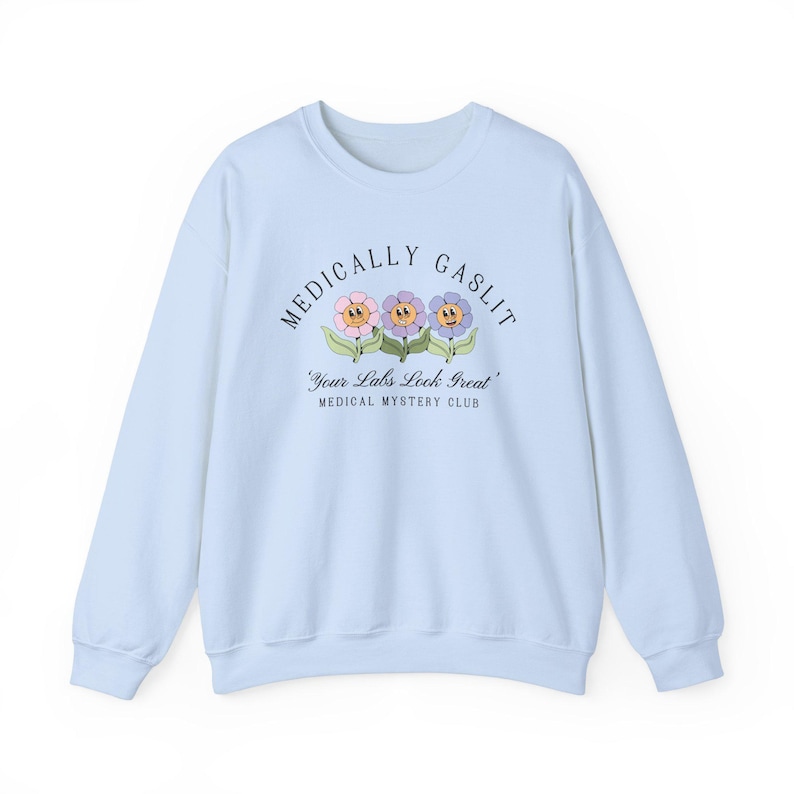 May include: Light blue sweatshirt with the text "Medically Gaslit" and a graphic of three cartoon flowers with faces. The text below the graphic reads "Your Labs Look Great" and "Medical Mystery Club".