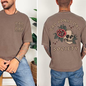 May include: A brown t-shirt with the text "Rad Bonus Dad Society" and a skull and rose graphic.