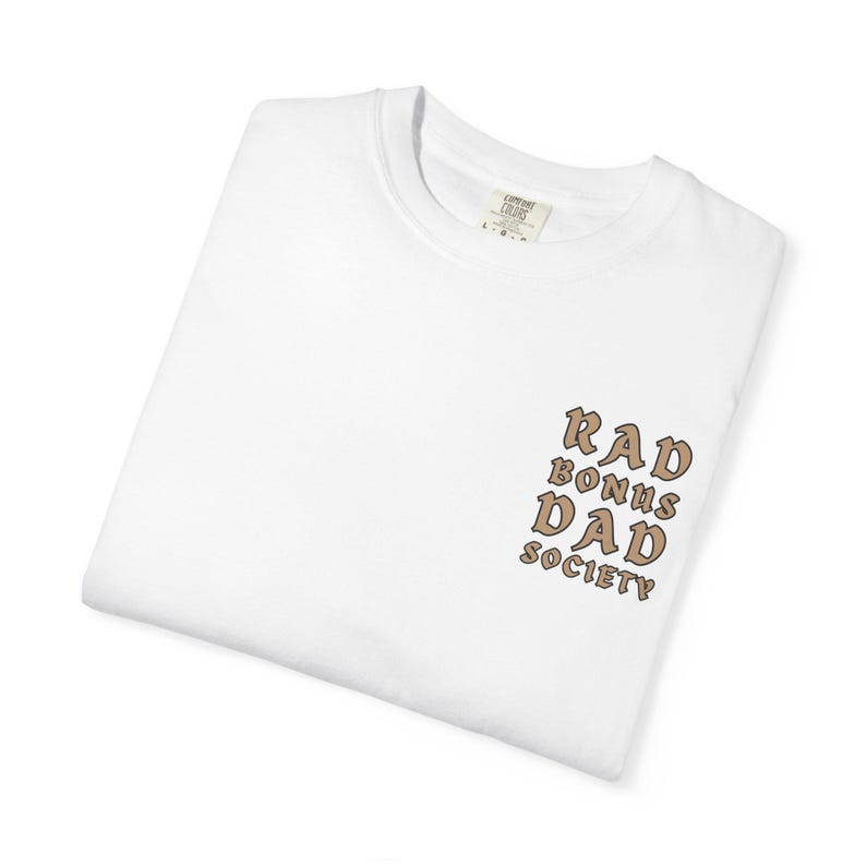 May include: White t-shirt with a brown graphic that says "Rad Bonus Dad Society" on the front.