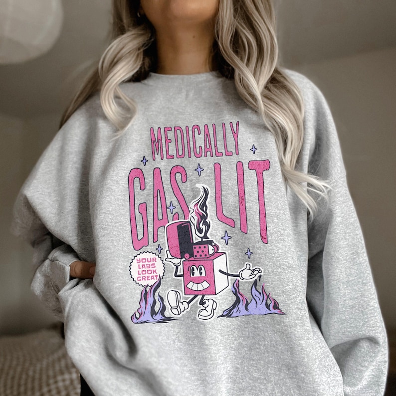 Pode incluir: Camisola cinzenta com um gr&aacute;fico rosa de um isqueiro de desenho animado com chamas e o texto "Medically Gaslit" e "Your Lads Look Great".