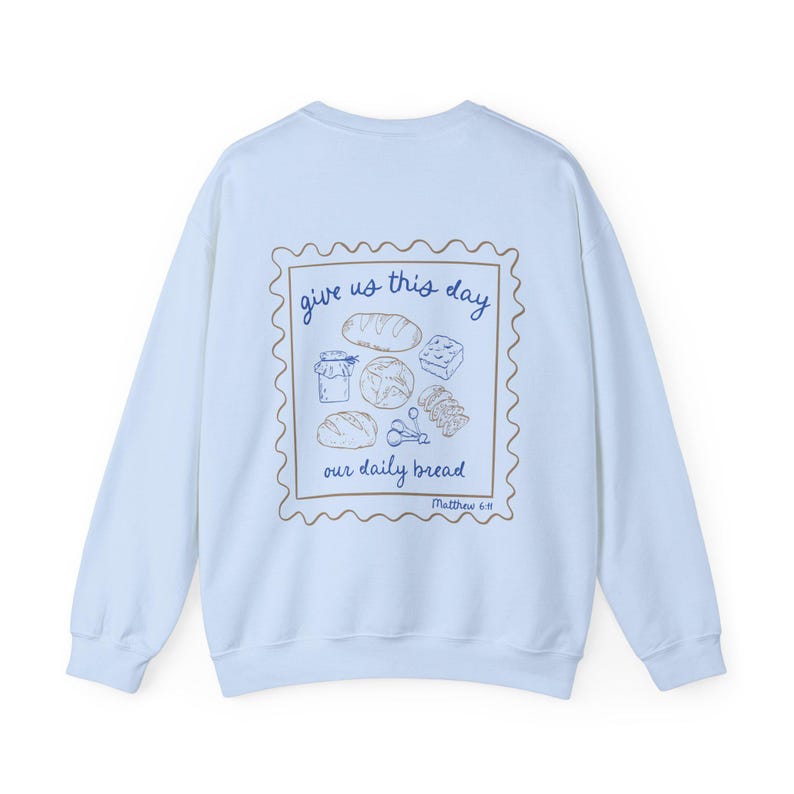 May include: Light blue sweatshirt with a graphic of a stamp with the text "give us this day our daily bread" and a drawing of bread and other food items. The text "Matthew 6:11" is below the stamp.