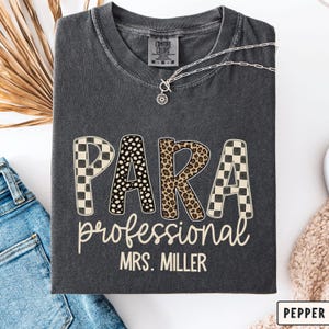 May include: A charcoal gray t-shirt featuring the word PARA in large letters with checkered and animal print patterns. Below, the word professional is written in a script font, followed by the text MRS. MILLER in a simple sans-serif font.