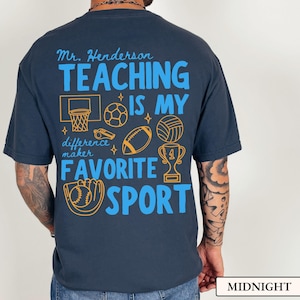 May include: Midnight blue t-shirt with a graphic design in blue and gold. The design includes the text "Mr. Henderson TEACHING IS MY FAVORITE SPORT" with sports-related icons such as a basketball hoop, soccer ball, and trophy.