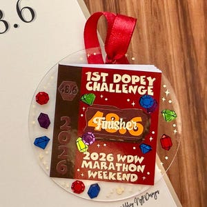 May include: A clear, round ornament with a red ribbon, featuring a design for the 1st Dopey Challenge and 2026 WDW Marathon Weekend. The ornament has a brown and red color scheme with the word "Finisher" and the number "48.6".