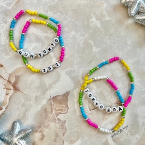 May include: Two colorful beaded bracelets with the words "RUN TOKYO 2022" and "TOKYO ERA" spelled out in white letters.