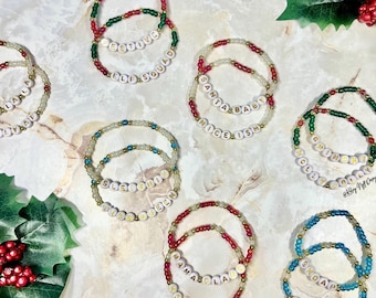 May include: A collection of beaded bracelets with holiday-themed words. The bracelets feature red, green, gold, and clear beads. The words include "Jolly", "Festive", "Santa Baby", "Nice-ish", "Ho Ho Ho", and "Snowy".