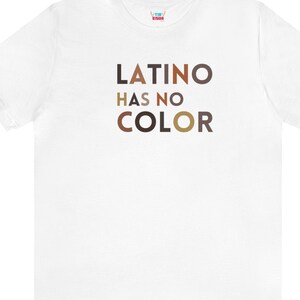 May include: White t-shirt with the text "LATINO HAS NO COLOR" in brown, tan, and light brown letters.