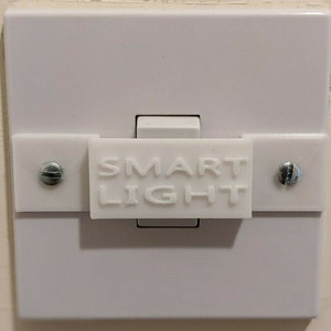 Pode incluir: Um interruptor de luz branco com uma cobertura de plástico branco que diz "SMART LIGHT".