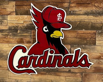 May include: A red, black, and white Cardinals logo featuring a cardinal bird wearing a baseball cap with the letter "S". The word "Cardinals" is written in a cursive font. The logo is mounted on a textured, multi-colored stone wall.