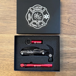 May include: A black gift box with a white emblem and the text "Cluster Springs F.D. Halifax Co. VA". Inside, a black multi-tool, a red flashlight, and a red key chain tool are visible.