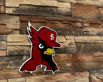 May include: A red and black cardinal bird logo with a white outline, wearing a red baseball cap with a white "$" symbol. The logo is mounted on a textured, multi-colored stone wall.