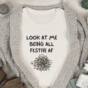 May include: White t-shirt with the text "Look at me being all festive af" and a tangled string of Christmas lights.