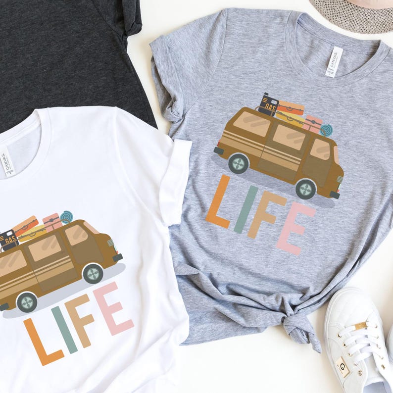 May include: White and gray t-shirts with a brown van graphic carrying luggage and the word "LIFE" in colorful letters. The shirts are casual wear, perfect for travel enthusiasts.