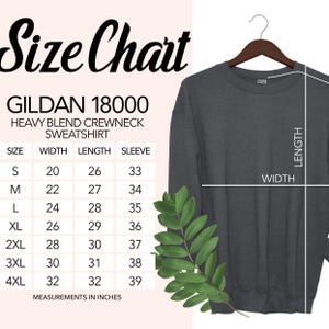 May include: A dark gray Gildan 18000 heavy blend crewneck sweatshirt hanging on a wooden hanger. A size chart is displayed, showing measurements in inches for sizes S to 4XL. The chart includes width, length, and sleeve measurements.