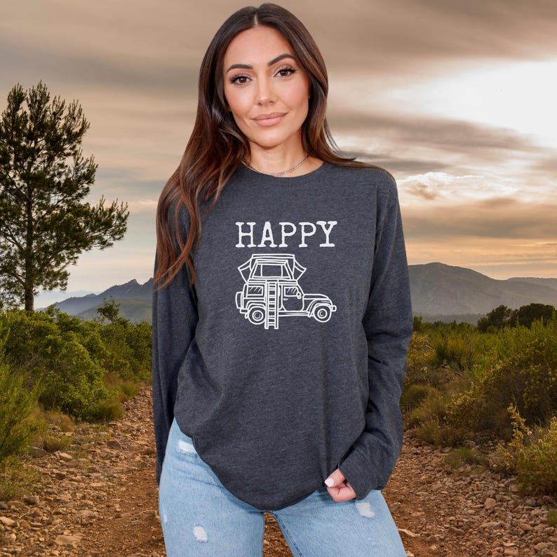 May include: A dark grey long-sleeved shirt with the word "HAPPY" printed in white on the front. A white outline of a car with a tent on top is printed below the word "HAPPY".