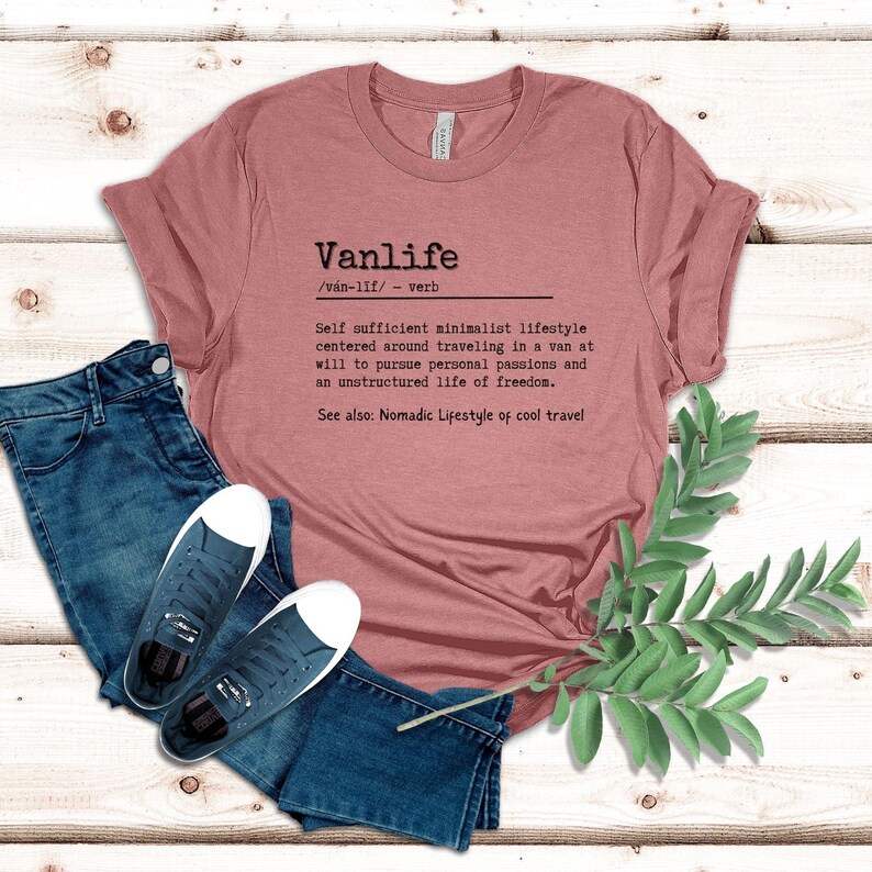 Puede incluir: Una camiseta rosa polvorienta con un estampado gr&aacute;fico negro que define "Vanlife" como un estilo de vida minimalista autosuficiente centrado en viajar en una furgoneta. El texto tambi&eacute;n dice "Ver tambi&eacute;n: Estilo de vida n&oacute;mada o viajes geniales."