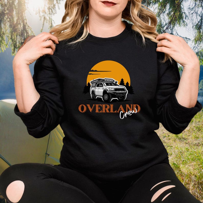 May include: Black sweatshirt featuring an orange sunset graphic and a white truck with a roof rack. The text "Overland Crew" is printed in orange below the truck.