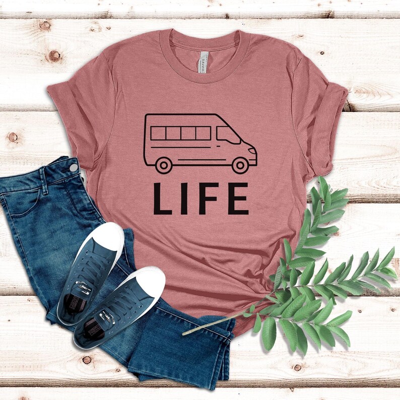 Op de afbeelding: Een roze T-shirt met een zwarte omtrek van een bestelwagen en het woord "LIFE" erop gedrukt.