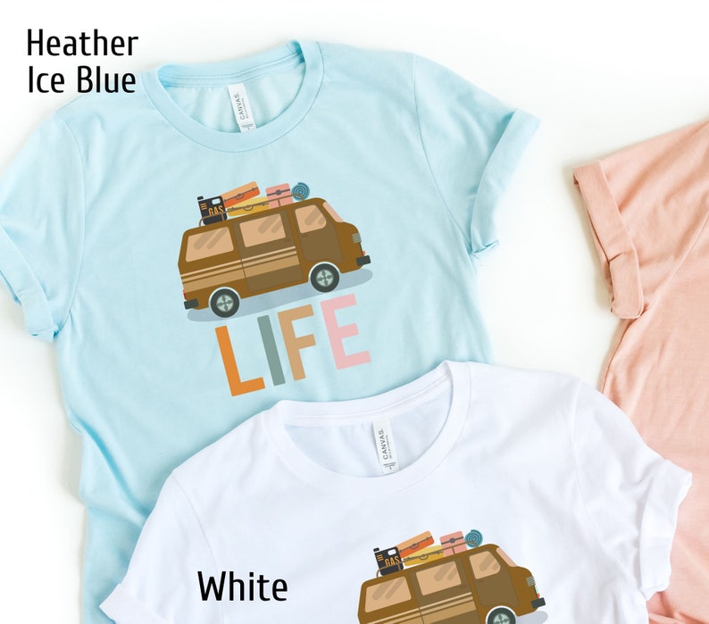 May include: Light blue t-shirt with a brown camper van graphic and the word "LIFE" in orange, gray, and pink. The van has luggage on top. The shirt is made of a soft material.