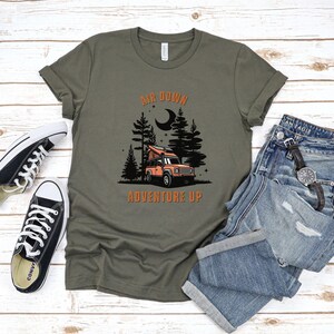 May include: A green t-shirt with the text "Air Down Adventure Up" in orange. The design features a black silhouette of a forest with a moon and a red truck with a pop-up tent.